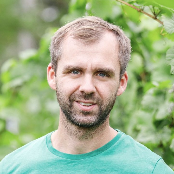 Rico Leonhardt steht lächelnd zwischen Weinreben